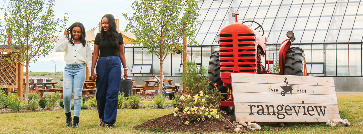 woman holding daughter's hand while walking beside Rangeview community sign that sits in front of a tractor 